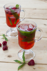 Raspberries fresh drinks with ice and mint on wooden table, selective focus