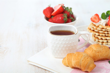 Tea with croissants and fresh strawberries on the table