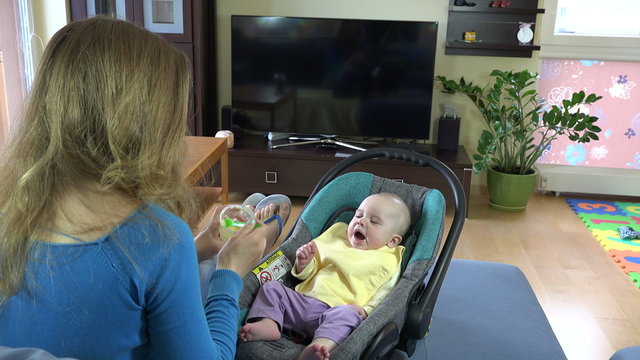 sleepy little 5 month baby girl eat vegetable pap with young mother in room. Static tripod shot. 4K UHD video clip.
