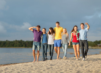 group of happy friends walking along beach