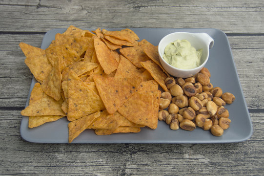 pecking on a plate, tortilla chips, kikos and guacamole.