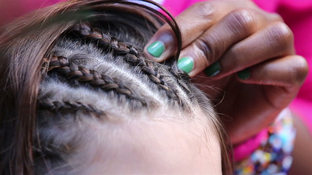 Traditional African braids. Woman braids hair girl on the street.