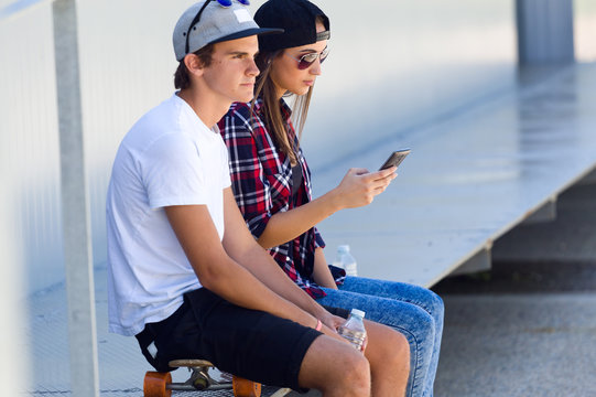 Two skaters using mobile phone in the street.