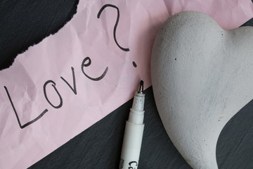 Hand-written text Love? on a piece of wrinkled paper, one heart of stone and a pencil  