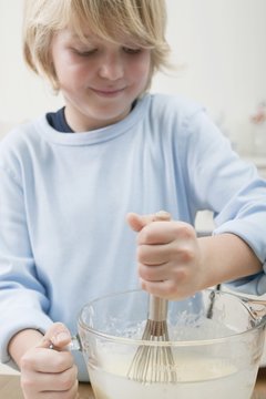 Boy stirring baking mixture in glass bowl with whisk