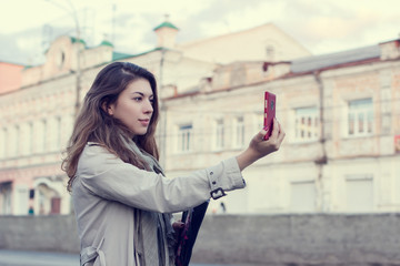 Young woman taking pictures on the smartphone while walking through the streets of the city.