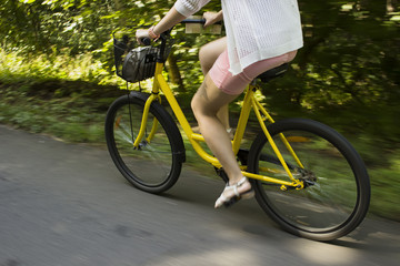 Fototapeta na wymiar Riding yellow bicycle on the forest road. Close-up of young woman riding bicycle