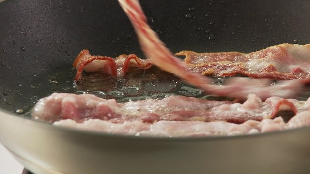 Rashers of bacon being fried and turned in a pan