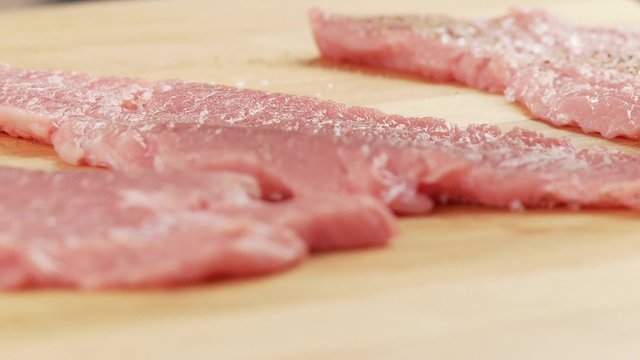 Tenderised veal escalopes being turned and seasoned with salt and pepper