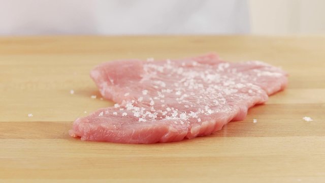 Tenderised veal escalopes being seasoned on both sides with salt and pepper