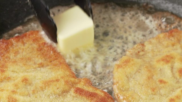 Breaded escalopes being fried in a pan with a knob of butter being added to the pan