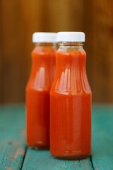 Two bottles of homemade ketchup on turquoise wooden table select
