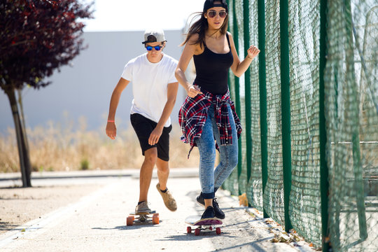 Young Couple Skateboarding In The Street.