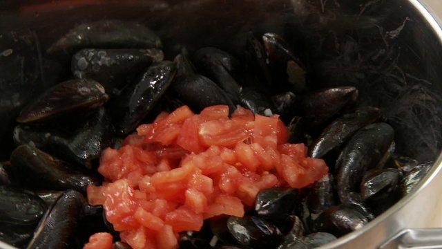 Tomato pieces being added to mussels and salted