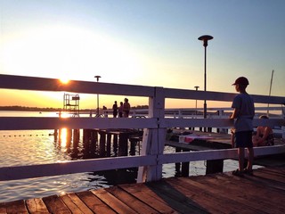 Chłopiec na molo patrzy na zachód słońca