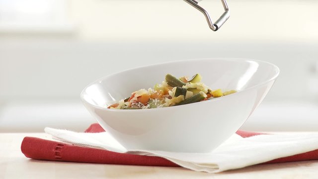 Minestrone being garnished with Parmesan