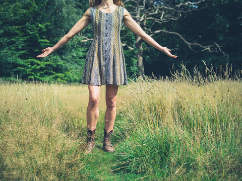 Young woman in dress raising her arms in meadow