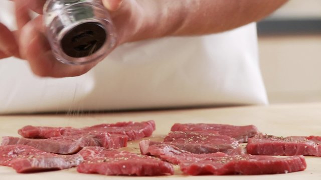 Veal escalopes being seasoned with pepper and salt
