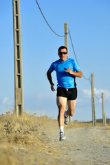 sport man with sun glasses running on countryside track with power line poles