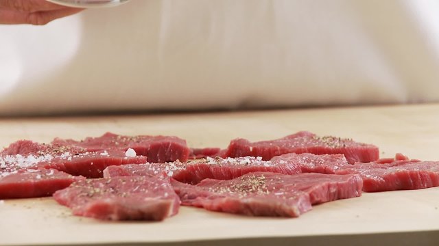 Veal escalopes being seasoned with salt