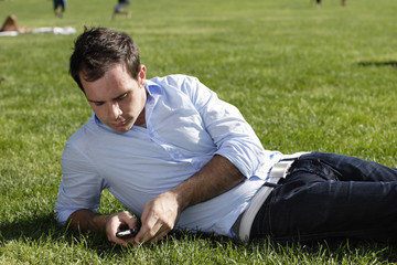 Naklejka na ściany i meble Man lying on grass checks his cell phone.