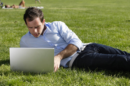 Man works on his laptop while lying on a grassy field.