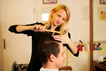 Female hairdresser cutting hair of smiling man client at beauty