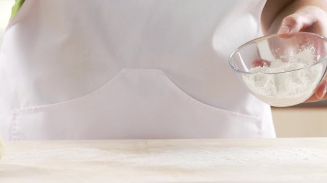 A work surface being sprinkled with flour and potato dough being rolled