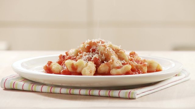 Gnocci with tomato sauce being sprinkled with Parmesan