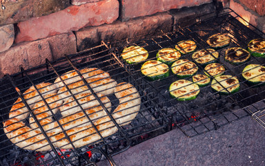 Sausages and zucchini cut into slices cooking on an outdoor grill.