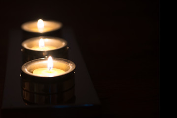 Three candles in silver holders in a row with a black background.  Selective focus and narrow depth of field has been used on the first of the three candles.