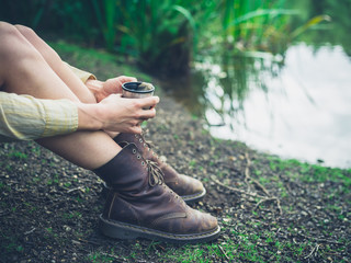Woman drinking tea by pond in forest