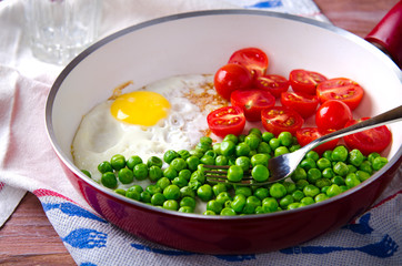 Breakfast with fried egg, green peas and cherry tomatoes