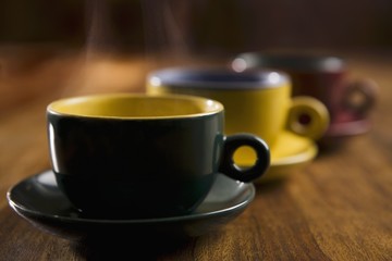 Steaming tea or coffee in three coloured cups and saucers