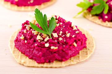 Beet hummus with peanuts and parsley on thin wafers