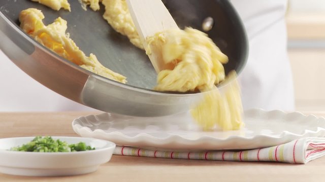 Scrambled eggs being put on a plate and sprinkled with herbs