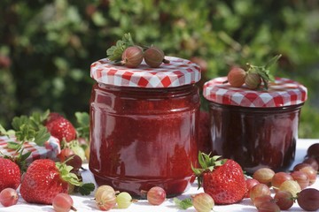 Two jars of strawberry and gooseberry jam and fruit