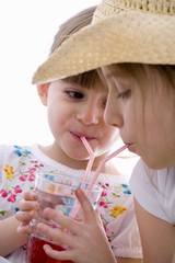 Two girls drinking fruit juice out of one glass with straws