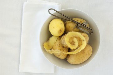 Potatoes and a peeler in a bowl