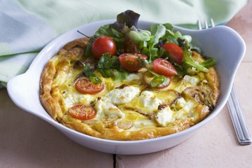 An omelette in a baking dish with goat's cheese and tomatoes