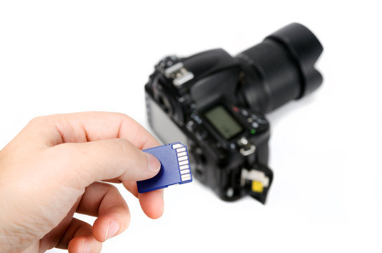 Hand holds SD Memory card - Flash card and DSLR camera on the background
