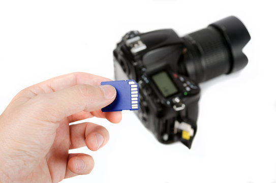 Hand holds SD Memory card - Flash card and DSLR camera on the background