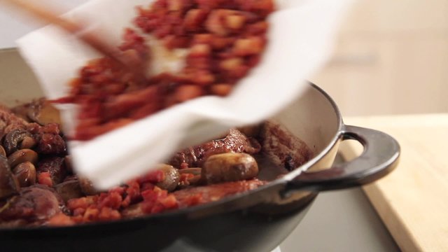 Fried bacon being added to coq au vin
