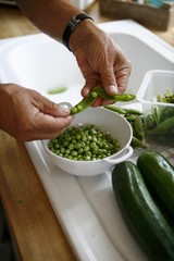 Peas being shelled and vegetables on a work surface