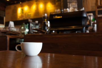 white cup of coffee on wooden bar in Coffee shop blur background