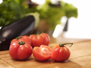 Tomatoes, whole and halved, on a chopping board with aubergine and salad