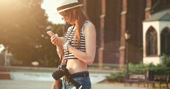 Woman using smartphone in the European city. Slow Motion, 4K. Hipster girl browsing Internet, searching for maps and information, communicating outdoors. Travel. Lens flare. 