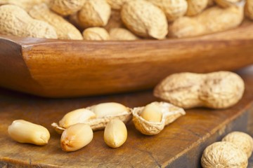 Peanuts, whole and shelled, in and in front of a wooden bowl