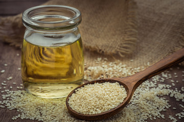Sesame seeds on wooden spoon and sesame oil in glass jar
