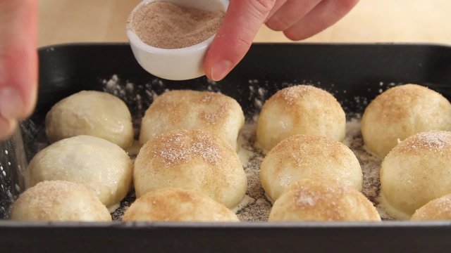 Raw Buchteln (baked, sweet yeast dumplings) being dusted with cinnamon sugar